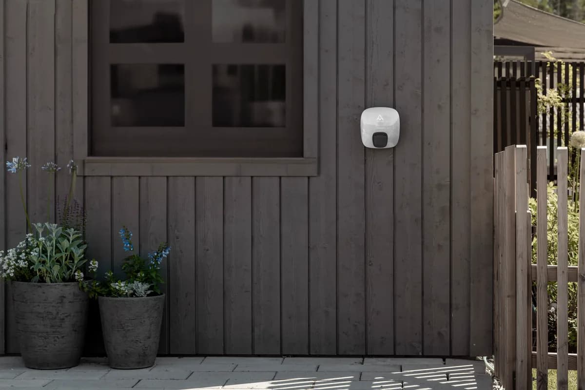 Charge Amps Luna with a white cover installed on the outside wall of a timber-clad home