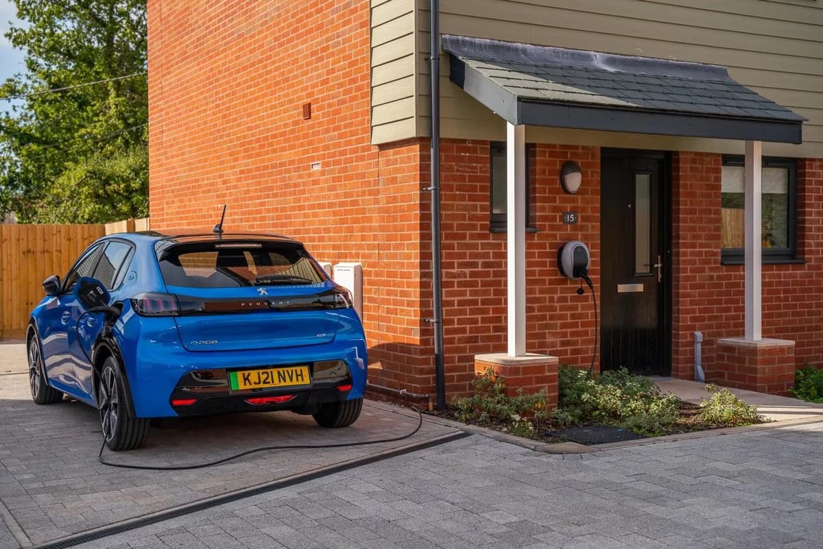 A blue electric car connected to a Solo 3 socket wallbox beside a home's front door